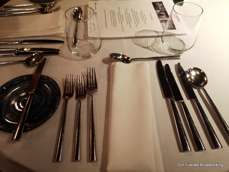 Image: A white napkin, and cutlery on a table, with two glasses, a menu and a side plate.